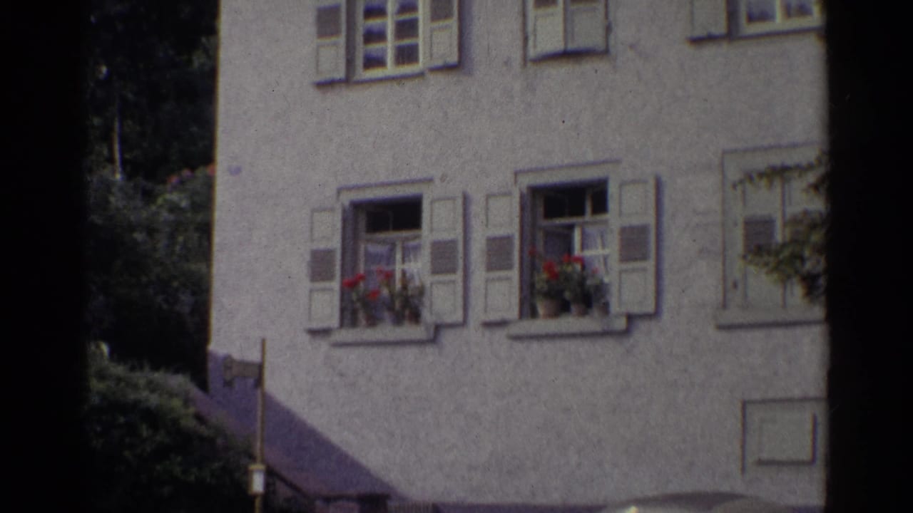 1961 Germany frame of a stucco building facade with shuttered windows, flower boxes, and a dark vertical edge from the film scan.