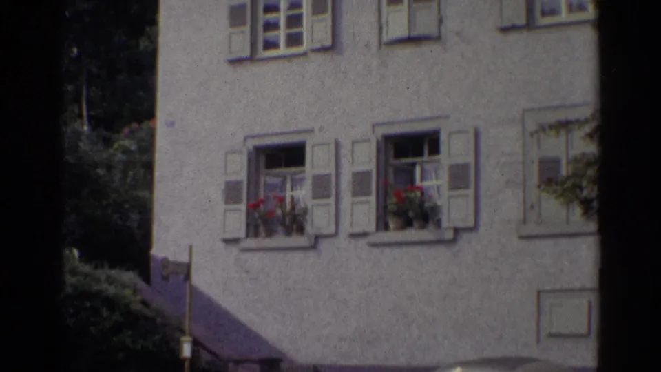 1961 Germany frame of a stucco building facade with shuttered windows, flower boxes, and a dark vertical edge from the film scan.