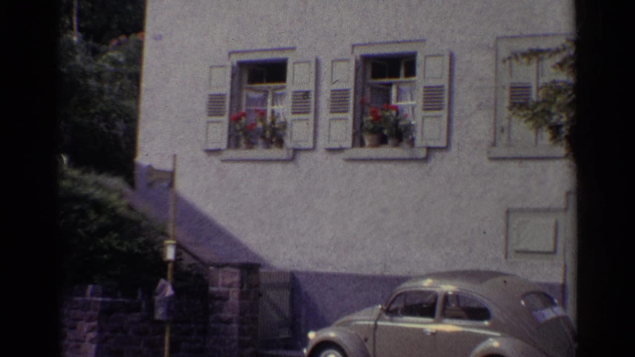 Volkswagen Beetle parked beside a stucco building with shuttered windows and flower boxes.