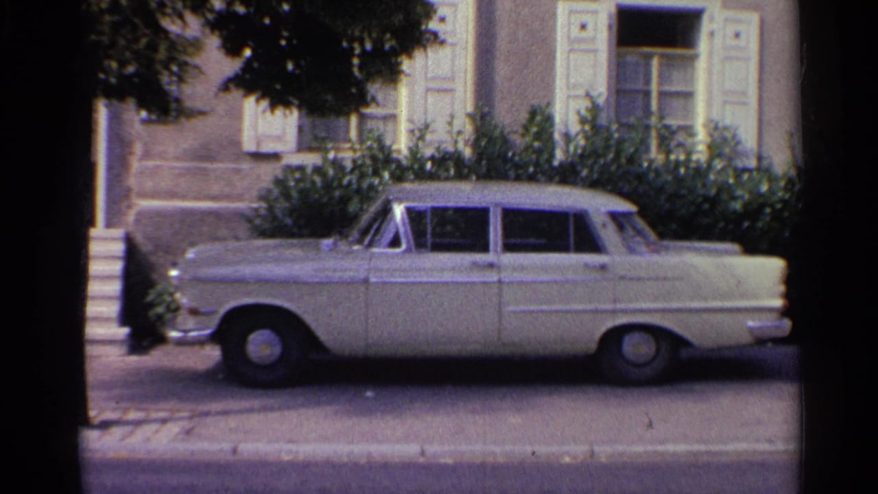 1961 Germany 8mm frame showing a white sedan parked along a residential street outside a shuttered house.