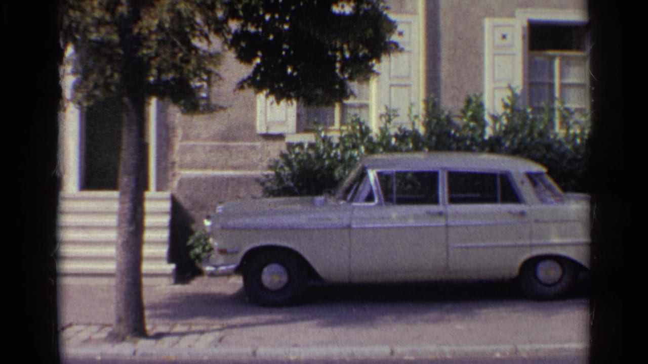 8mm view of a parked white sedan, front steps, tree trunk and shuttered house exterior in 1961 Germany.
