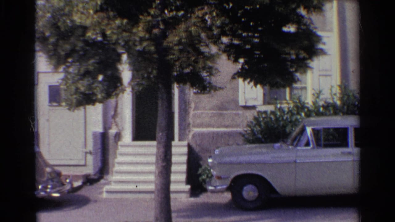 Light-colored sedan parked outside a stucco house with steps, shutters, and a tree in front.