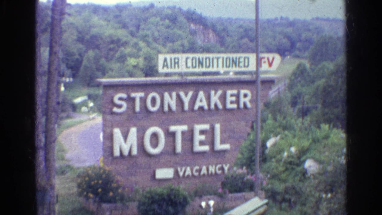 1961 home-movie frame showing a closer view of the Stonyaker Motel sign, with air conditioned and TV lettering above a landscaped roadside edge.