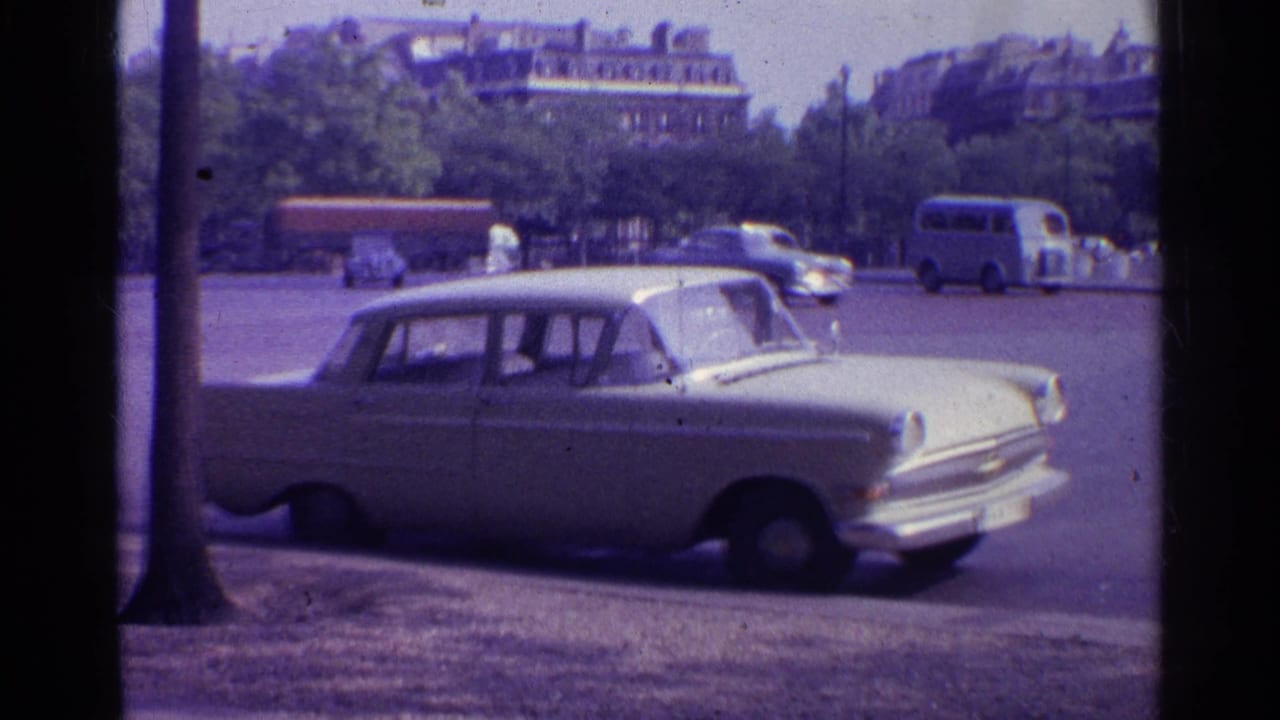 1961 Paris 8mm frame showing a white sedan at the curb, with trees, passing vehicles, and city buildings in the background.
