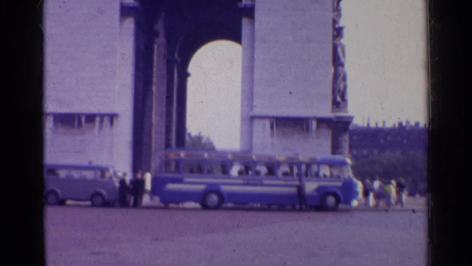 1961 Paris frame showing the Arc de Triomphe at street level, with a blue-and-white bus, small van, and pedestrians nearby.