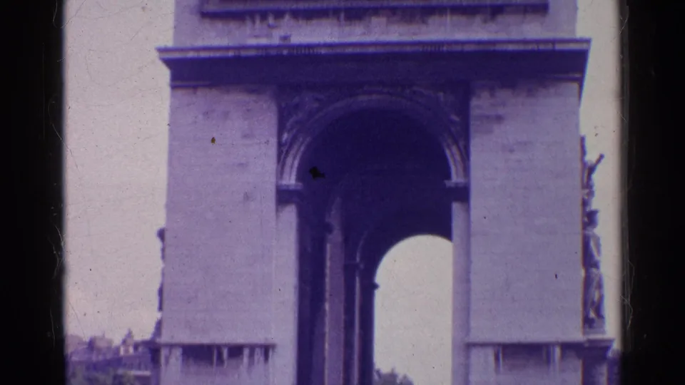 1961 8mm view of the Arc de Triomphe in Paris, framed higher on the stone facade with the arch opening and side sculpture visible.