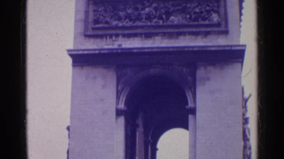 1961 Paris 8mm frame tilted toward the upper Arc de Triomphe, showing the relief panel, cornice, and shadowed arch below.