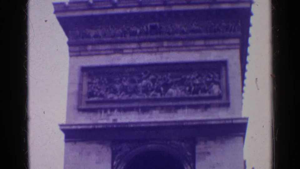 1961 Paris 8mm frame showing a lower close-up of the Arc de Triomphe, with carved reliefs, arch detail, film border, and purple color shift.