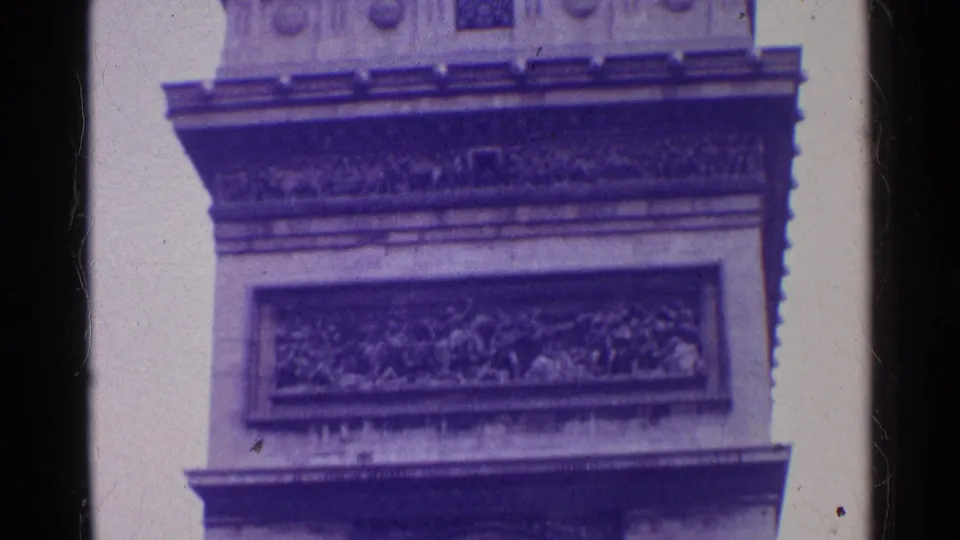 1961 Paris 8mm frame showing the Arc de Triomphe facade in close view, including relief panels, stone cornices, partial sculpture, and film wear.