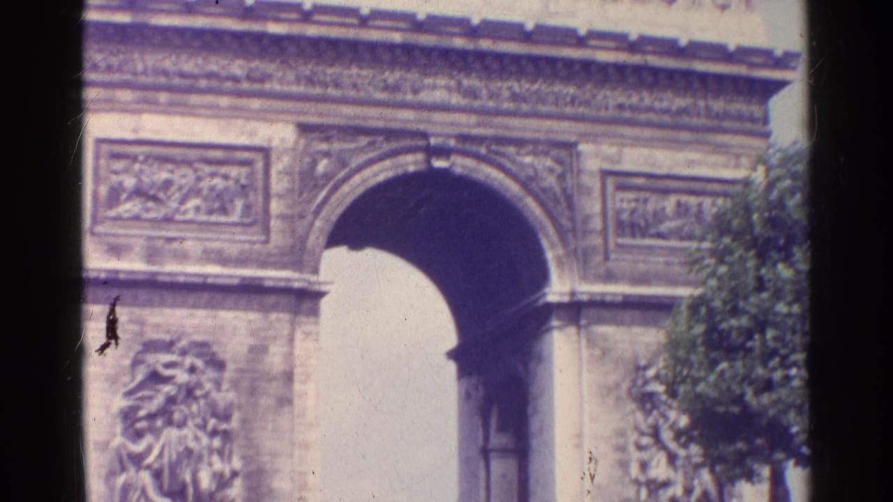 1961 Paris home-movie frame showing the Arc de Triomphe facade, central arch, carved panels, and a tree at the edge.