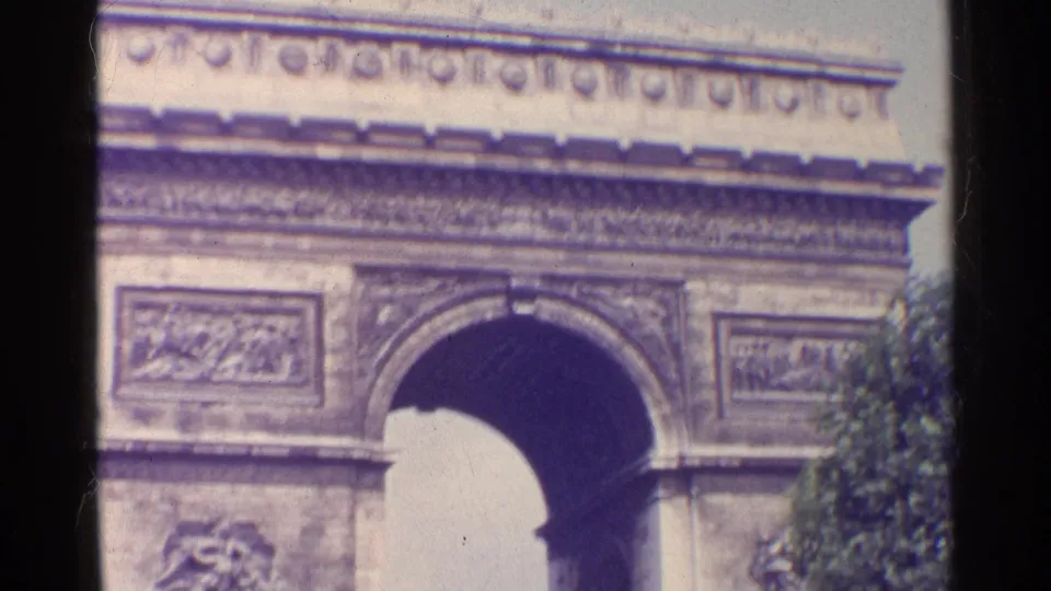 1961 Paris frame with the Arc de Triomphe arch cropped close, showing relief panels, frieze detail, and edge foliage.