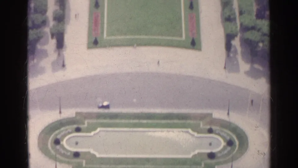 Elevated Paris garden view with geometric lawns, pale walkways, clipped plantings, and an oval ornamental area in soft 8mm color.