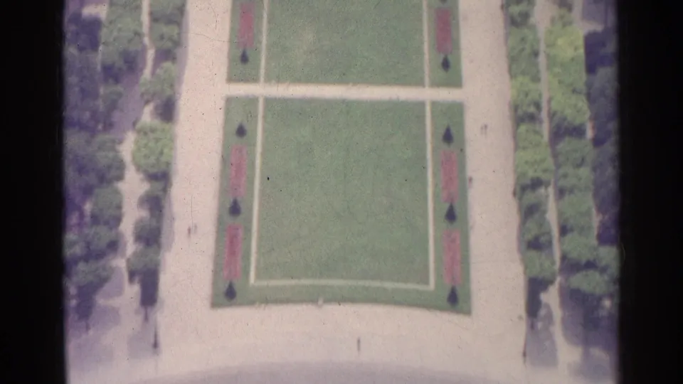 High-angle view of a formal Paris garden showing rectangular lawns, straight paths, dark shrubs, and tree-lined edges.