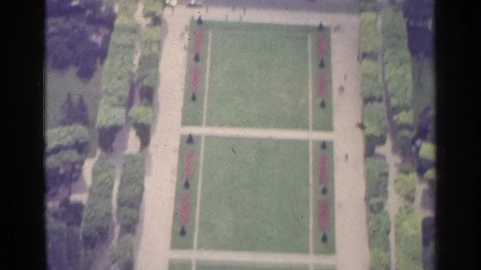 1961 Paris 8mm frame showing a formal garden from above, with green lawns, pale walkways, hedges, and small distant figures.
