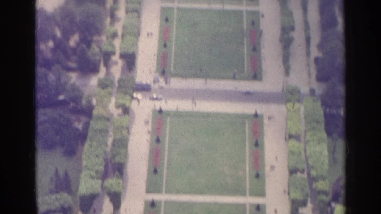 Elevated view of two formal lawn panels with paths, trees, and tiny people nearby.