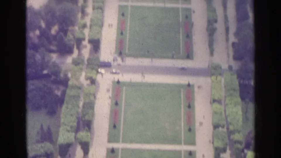 Aerial 8mm view in Paris showing symmetrical lawn panels, pale paths, clipped hedges, trees, and distant visitors.