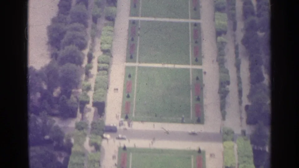 1961 Paris home-movie frame looking down over lawns, path grids, hedges, trees, and small people in a formal garden.