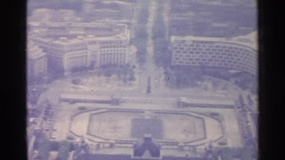 1961 8mm frame looking over Paris rooftops and roads toward the formal garden and palace-like structure below.