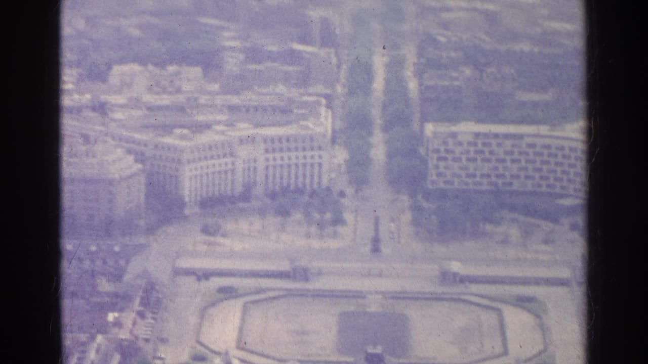 Aerial view of formal buildings, boulevard, and plaza seen through soft film grain.