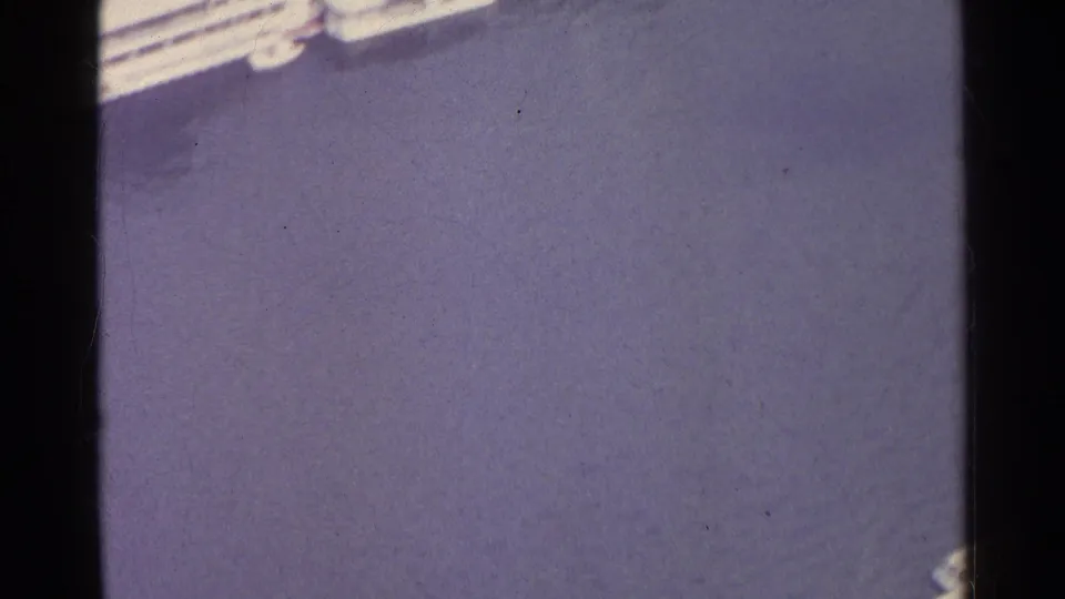 1961 8mm frame shifts from the Paris aerial view to rippling water beside a pale shoreline or embankment edge.
