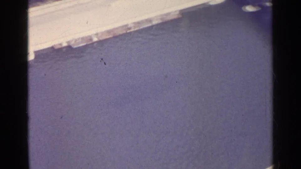 Final 1961 8mm frame shows textured water below a pale embankment or shoreline, retaining the faded home-movie look.