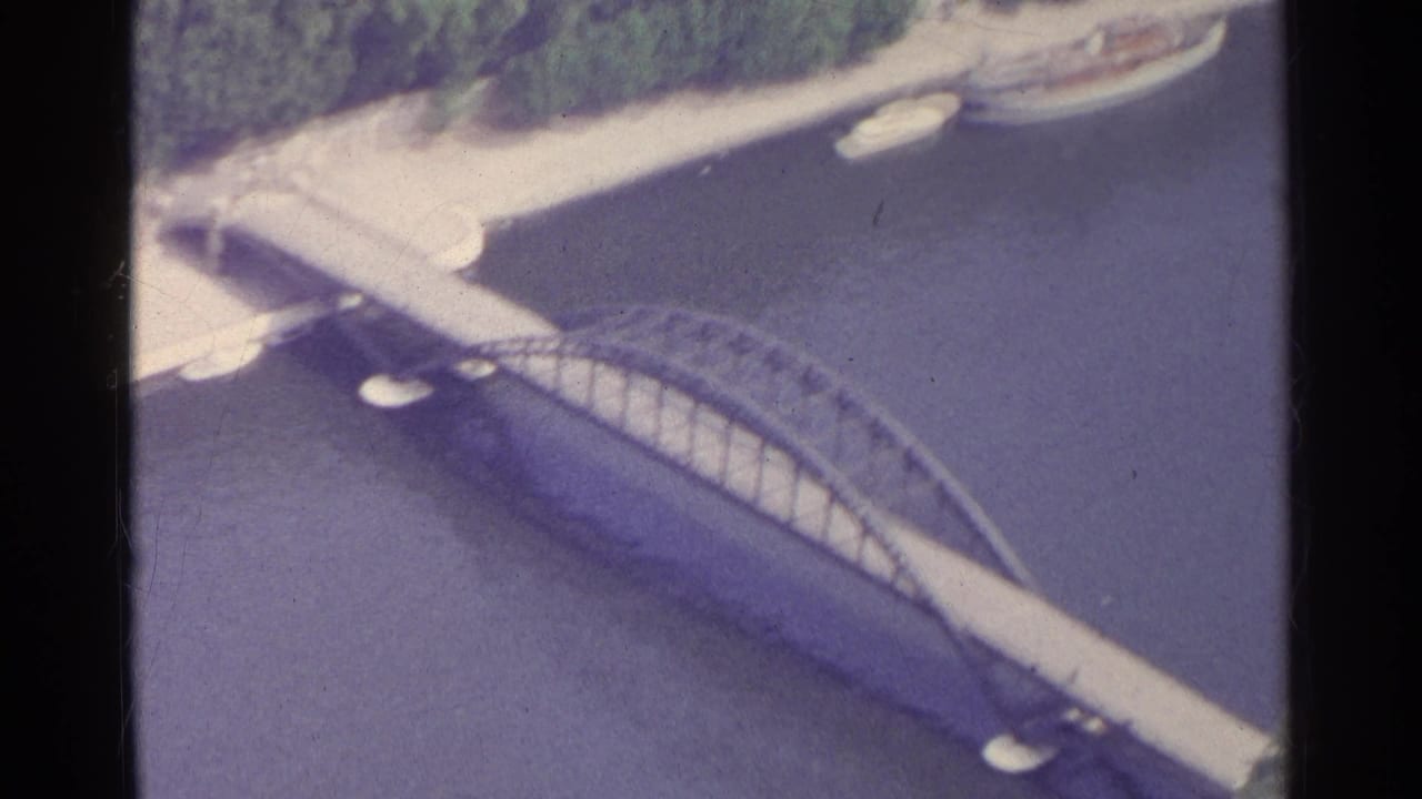 Aerial view of an arched bridge crossing a river beside a tree-lined bank.