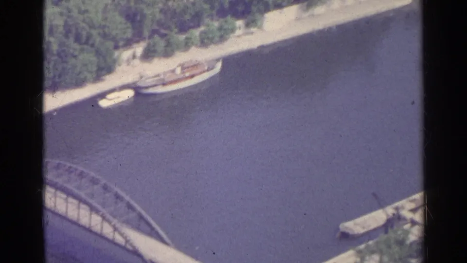 1961 Paris 8mm frame showing the river, a partial arched bridge, moored boats and a tree-lined bank from above.
