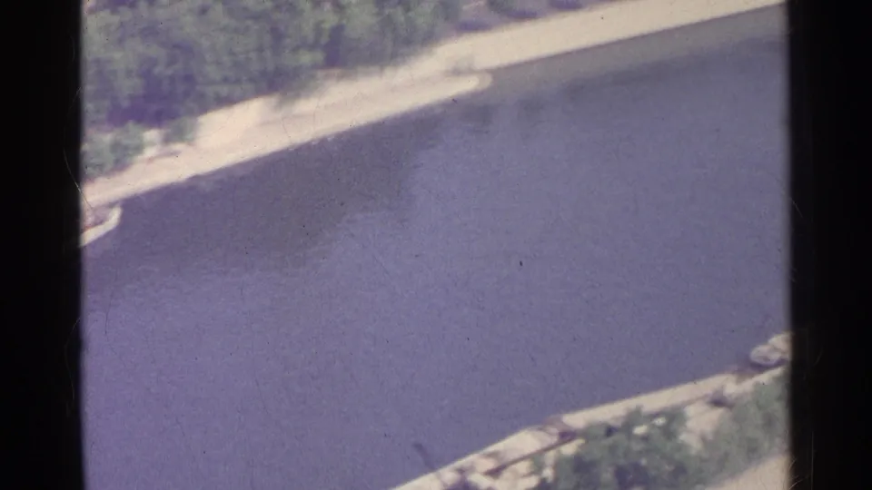 1961 Paris aerial home-movie view drifting across the river, with embankment, trees and faint boat shapes near the edges.