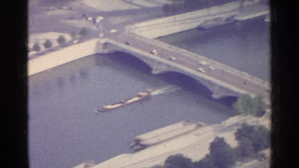 1961 Paris home-movie view of a bridge with traffic crossing while a barge travels along the river below.