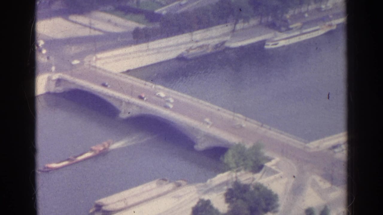 Aerial view of the Seine with an arched bridge, cars, boats, and riverside quays.