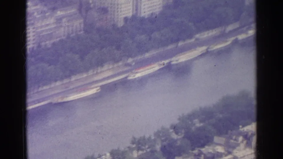 1961 Paris aerial home-movie frame with boats beside the Seine, riverside trees, embankment, and partial rooftops below.