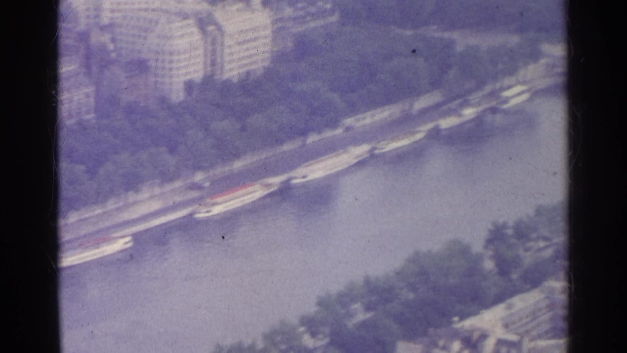 1961 Paris aerial 8mm frame showing the Seine, embankments, bridges, riverboats, and nearby urban buildings.