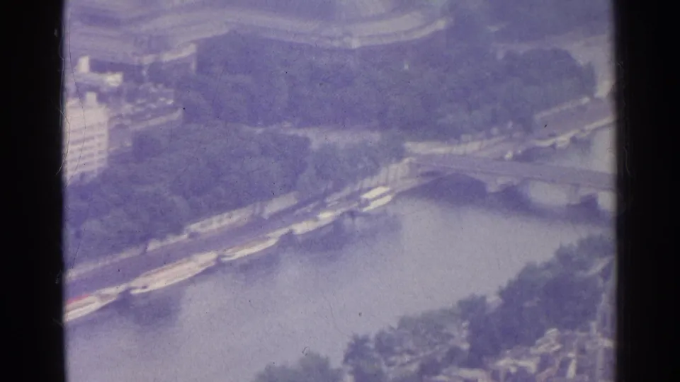Paris aerial home-movie frame with a purple cast, showing the Seine corridor, boats, bridges, trees, and riverside buildings.
