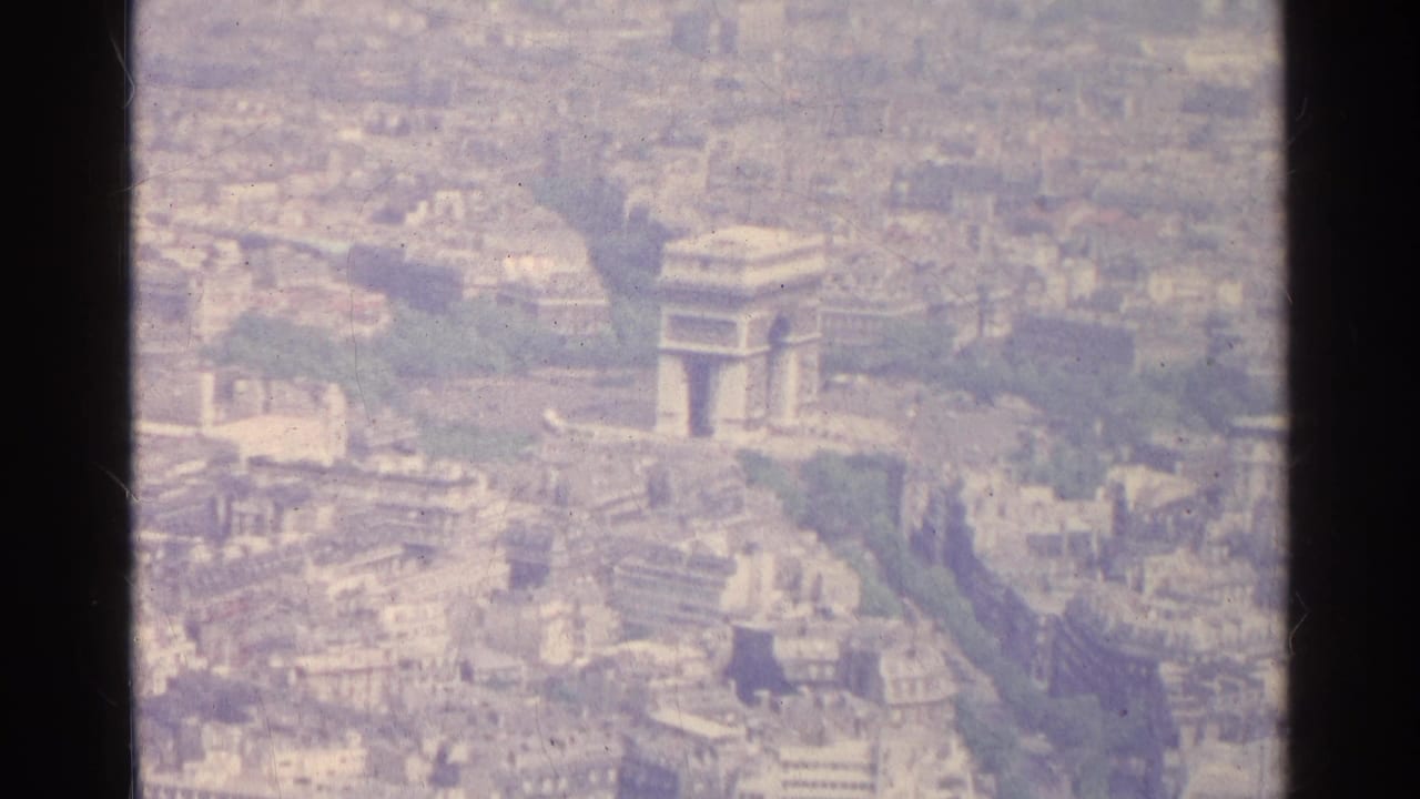1961 Paris aerial 8mm frame showing the Arc de Triomphe area surrounded by dense city blocks and green avenues.