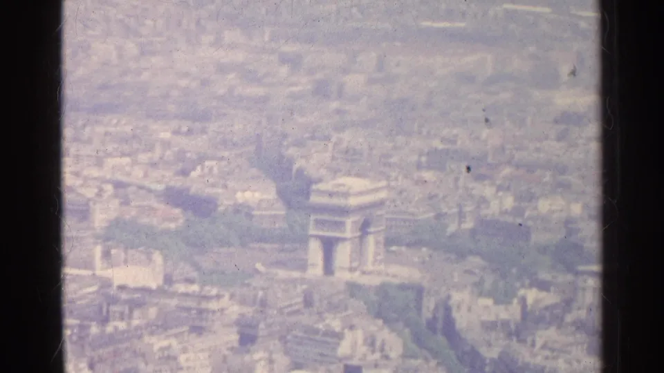 1961 Paris aerial frame with the Arc de Triomphe, surrounding avenues, and dense urban blocks visible through faded film color.