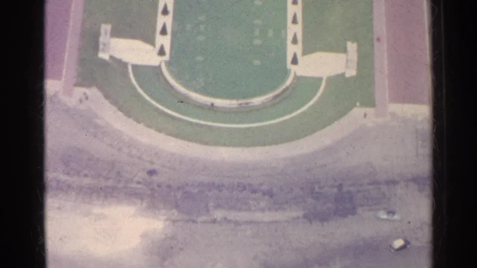 A 1961 Paris aerial frame shifts from the landmark view to a green marked ground surface with pale structures and surrounding pavement.