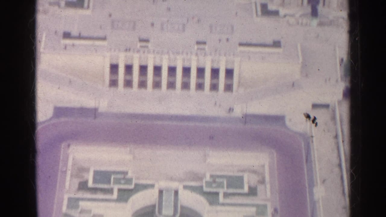 High-angle view of a broad plaza, facade, roofline, and part of a formal garden.
