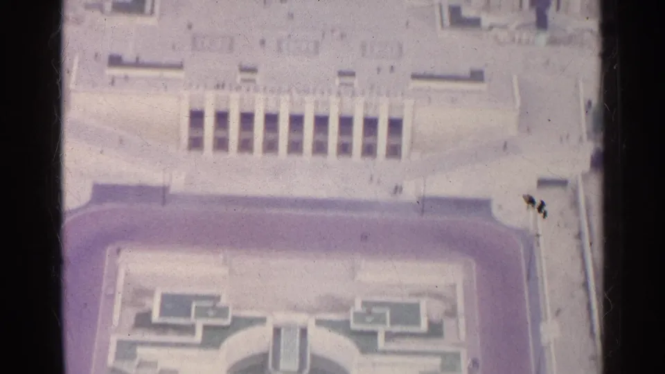 1961 Paris 8mm frame showing a broad pale plaza, monumental facade details, roof edges, and part of a formal garden below.