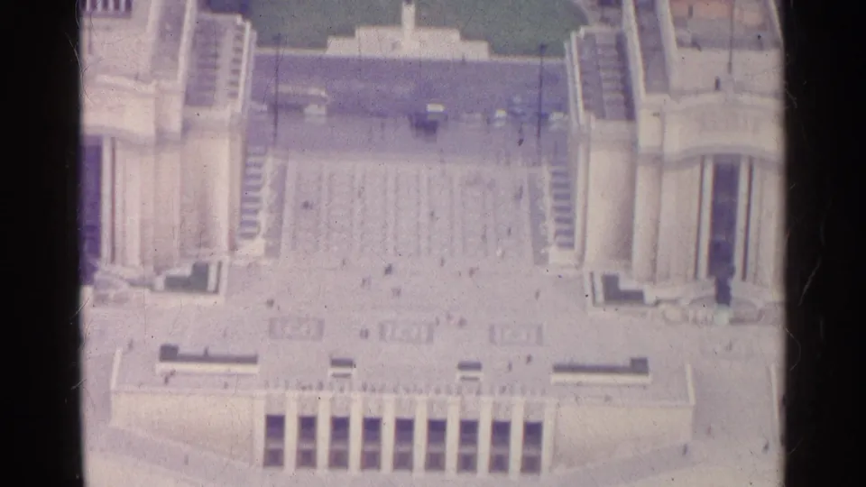 1961 Paris 8mm frame looking down on a large stone plaza framed by monumental buildings, stairways, and small moving figures.
