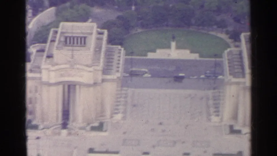 1961 Paris 8mm frame showing a monumental building beside a plaza, green lawn, trees, a central monument, and small vehicles.