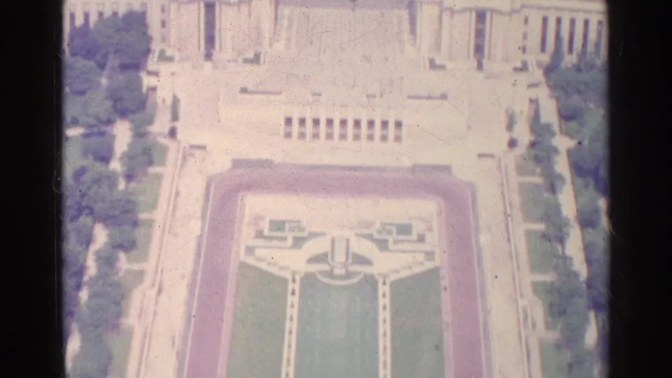 Faded 8mm aerial view of a Paris formal garden in 1961, with clipped lawns, terraces, and surrounding trees.