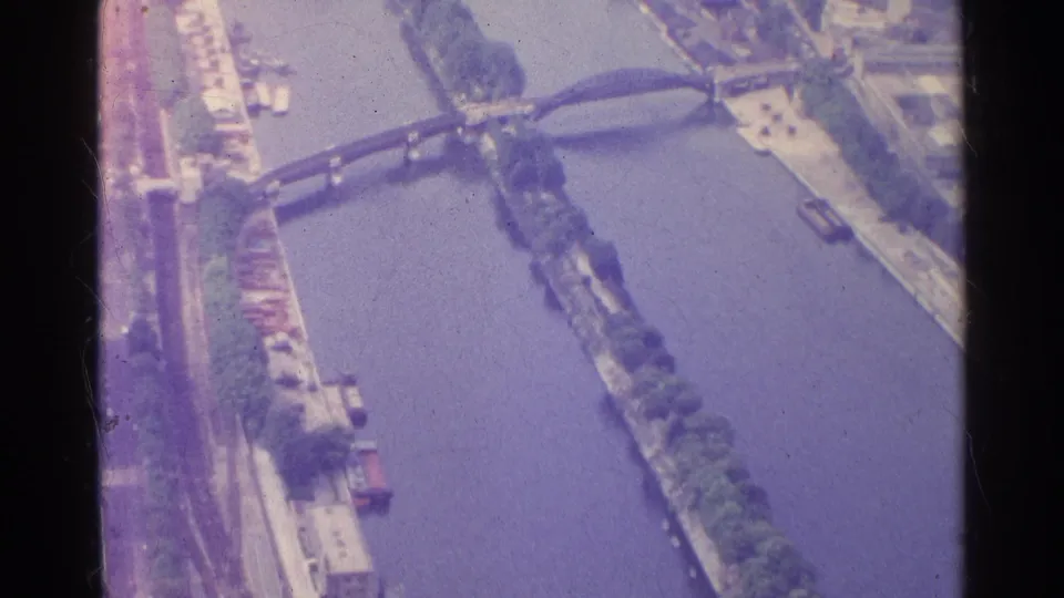 1961 Paris 8mm aerial frame looking along the Seine toward an arched bridge, with tree-lined banks and river traffic visible.