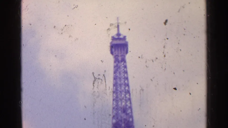 1961 Paris 8mm frame showing the Eiffel Tower from an elevated or aerial vantage, softened by haze and film wear.