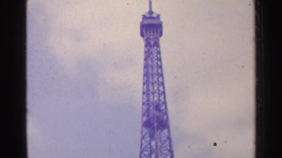 1961 8mm Paris home-movie frame showing the Eiffel Tower rising into a cloudy sky with dark film borders.