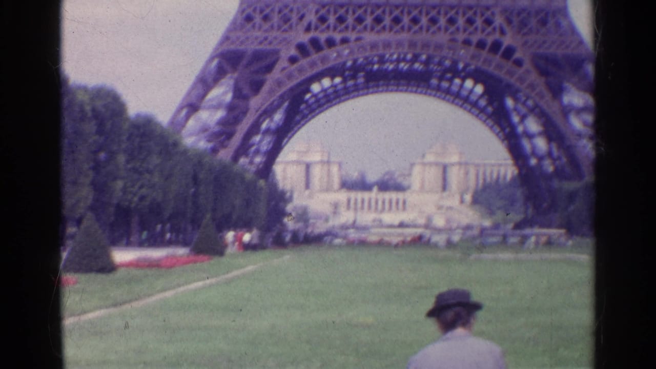 Eiffel Tower base over a green lawn with a visitor in a hat in the foreground.
