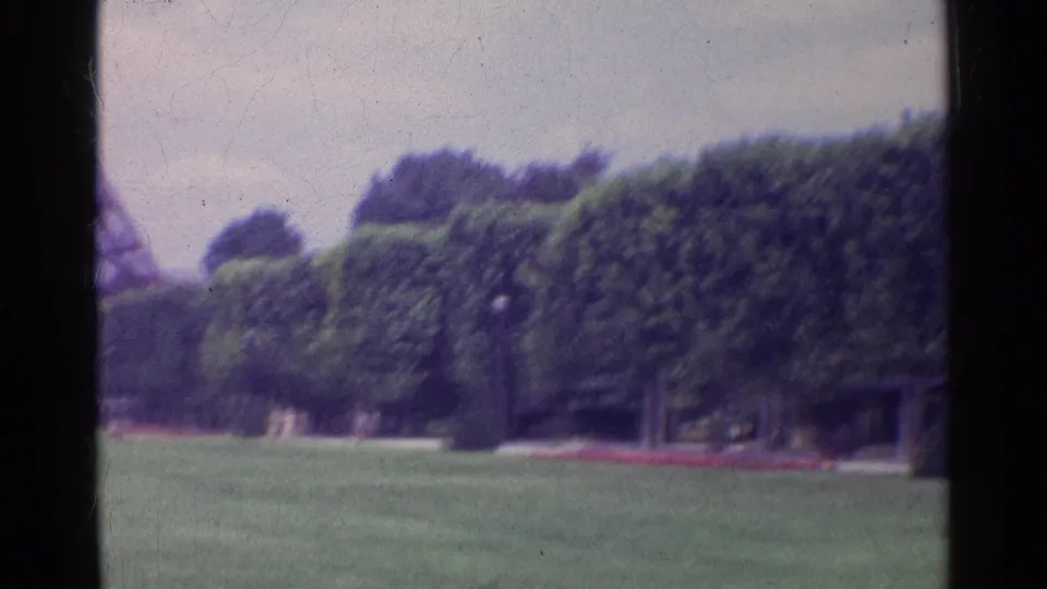 1961 Paris 8mm frame panning away from the tower toward formal trees, lawn, paths, and a red flower bed.