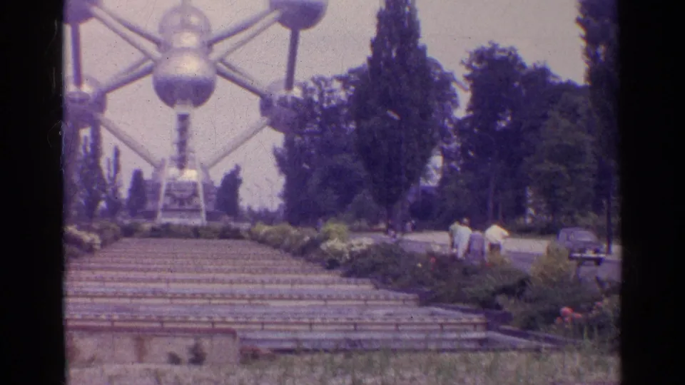 The Atomium appears beyond stone steps and formal planting beds, with visitors walking at the side.