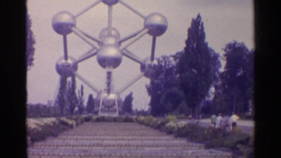 A closer 8mm view of the Atomium shows its silver spheres above steps, trees, garden beds, and visitors.