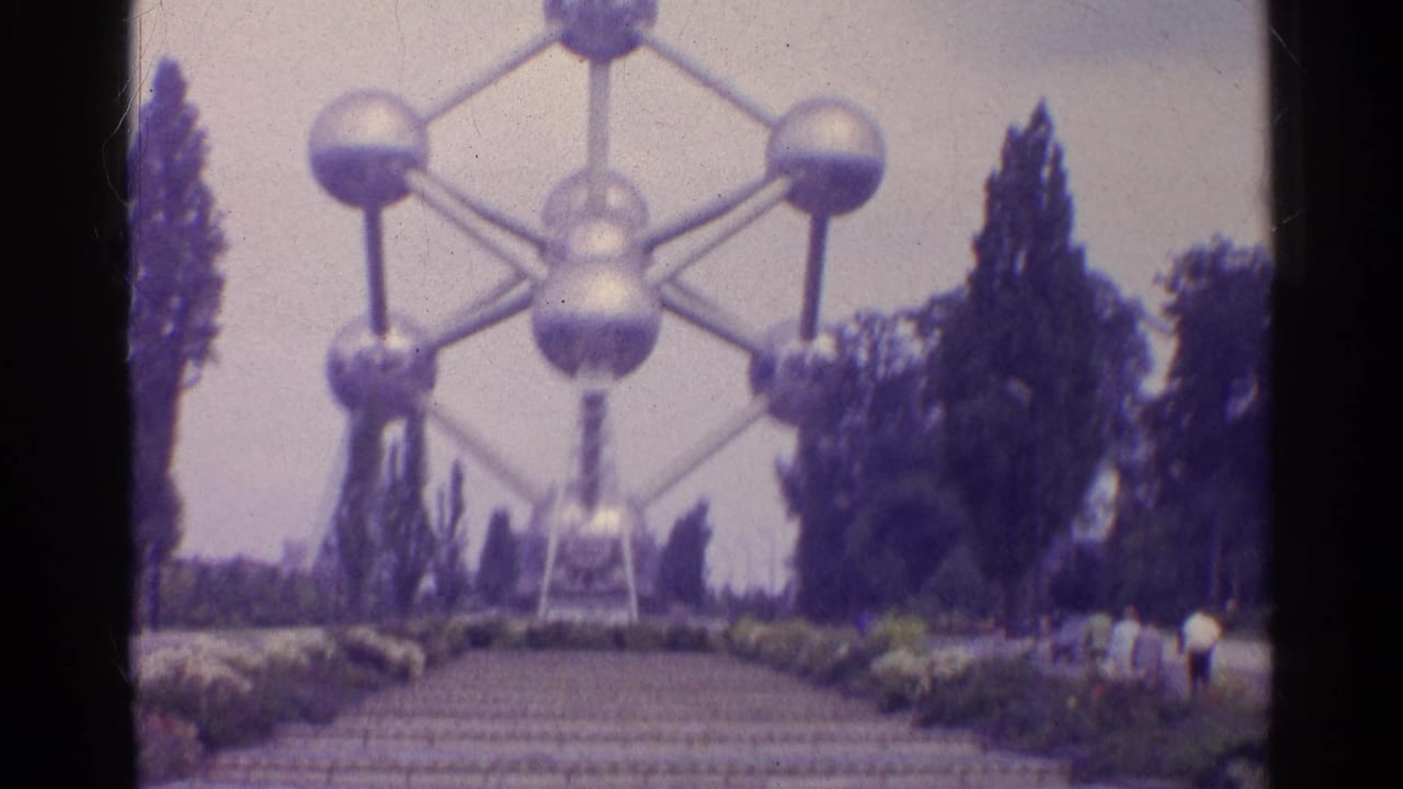 1961 8mm frame of a large silver interconnected-sphere landmark, with a path, trees, and distant visitors.