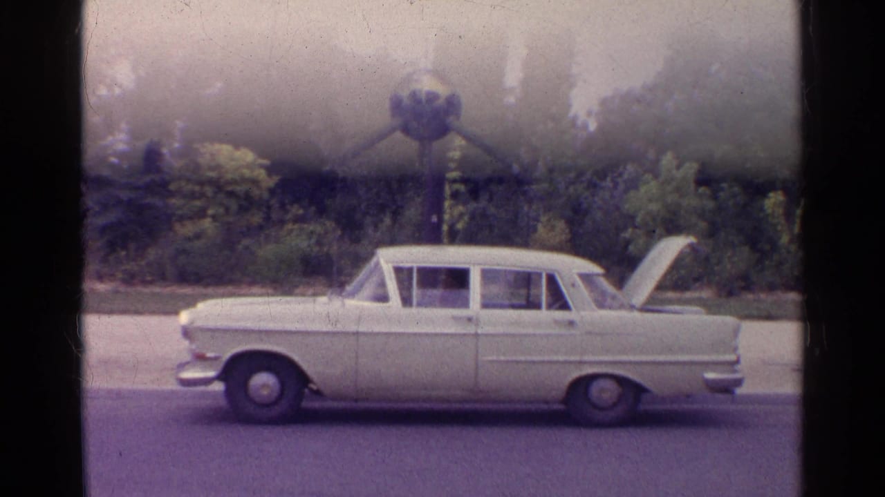 White classic sedan parked on a roadside with its trunk open.